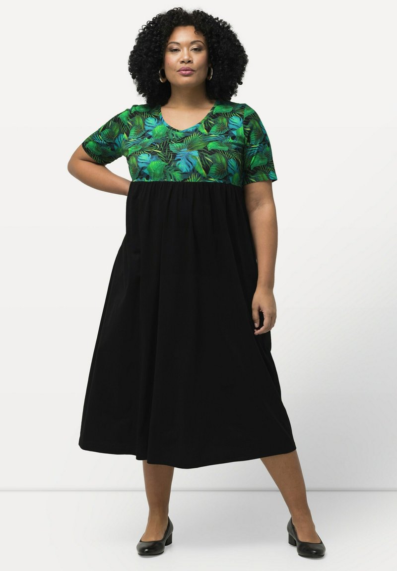Vestido maxi con parte superior de estampado de hojas tropicales verdes y falda negra plisada. Mangas cortas, escote redondo y silueta fluida.