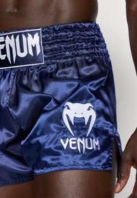 Tumši zila satīna šorti ar sakravātu jostasvietu, ar baltu izšūtu "VENUM" logotipu un stilizētu baltu logotipu apakšējā kreisajā kājā.