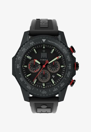 Black Timex watch with a textured rubber strap, round case, green luminescent hour markers, red accents, and multiple sub-dials.