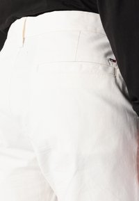 Witte katoenbroek met een achterzak en een klein logopatch met rode en blauwe accenten. Gladde textuur met een getailleerde pasvorm.
