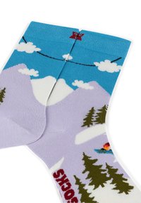 Chaussettes violettes avec des motifs de montagnes et de ski, bande supérieure bleue, nuages blancs et arbres verts. Présente une texture côtelée et des couleurs contrastées.