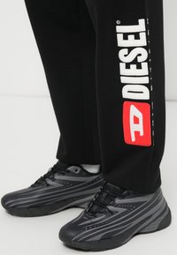 Μαύρο παντελόνι φόρμας με λευκό λογότυπο "DIESEL" και κόκκινο λεπτομέρεια. Μαύρα αθλητικά παπούτσια με γκρι σχεδιασμό ρίγες και παχιά σόλα.