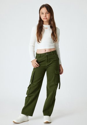 Groene cargo broeken met zijzakken, gecombineerd met een witte geribbelde langsmouw crop top met een hartvormige uitsnede bij de halslijn. Witte sneakers.