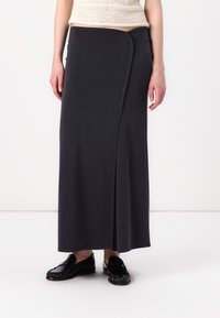 Lång svart kjol med en inslagningdesign, mjukt tyg, sidospalt och slät textur. Bärs med svarta loafers.