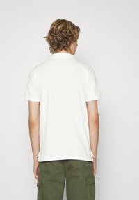 Hvid polo skjorte med korte ærmer og klassisk krave, parret med olivengrønne cargo shorts. Glat tekstur og rent design.