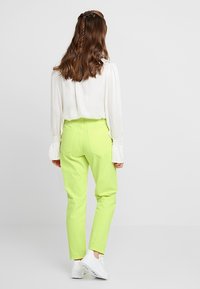 Pantalones livianos y vibrantes de color verde lima con corte recto, bolsillos traseros y cierre de botón, combinados con una blusa de manga larga blanca.