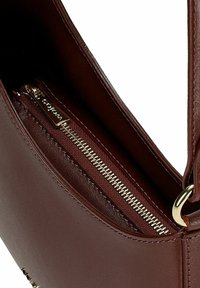 Hnědá kožená kabelka s vnitřní kapsou na zip. Obsahuje zlaté kovové doplňky a hladkou texturu. Navržena pro funkčnost a styl.