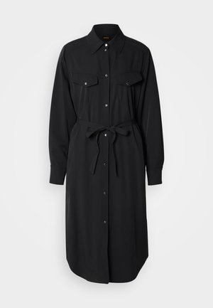 Svart, langermet skjortekjole laget av glatt stoff. Har to brystlommer, knappestolpe foran og stoffbelte i midjen.