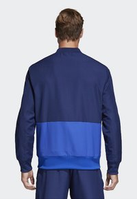 Herrenjacke in Marineblau mit einem einfarbigen blauen unteren Bereich. Verfügt über ein strukturiertes Design, eine glatte Textur und einen hohen Kragen.