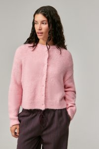 Helles pink, flauschiges Cardigan mit rundem Ausschnitt, Knopfverschluss und geripptem Saum. Kombiniert mit gestreiften, dunklen Hosen.