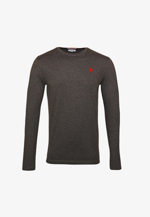 T-shirt à manches longues gris foncé avec un col rond, arborant un petit logo rouge. Associé à un jean bleu clair et des baskets sombres.