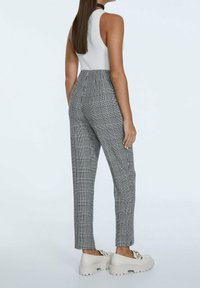 Zwart-wit geruite broek met hoge taille en taps toelopende broekspijpen, gecombineerd met chunky witte plateau schoenen.