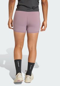 Σφιχτά, ανοιχτό μοβ αθλητικά σορτς με αντίθετη ραφή. Φοριούνται με μαύρες κάλτσες μέχρι το γόνατο και μπεζ αθλητικά παπούτσια.