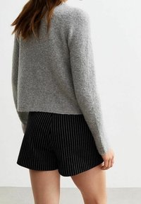 Grauer, strukturierter Pullover mit langen Ärmeln, kombiniert mit schwarzen Shorts mit Nadelstreifen. Der Pullover hat eine lockere Passform und endet knapp oberhalb der Shorts.