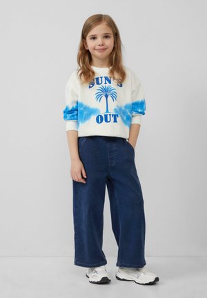 Biały sweatshirt z niebieskimi rękawami w stylu tie-dye, z grafiką palm tree i niebieskim napisem "SUN'S OUT", połączony z szerokimi dżinsami i trampkami.
