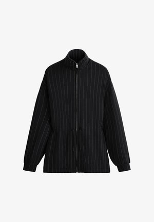 Fekete cipzáras dzseki vékony, függőleges fehér tűcsíkokkal, magas gallérral, húzózsinóros derékrésszel és hosszú, mandzsettás ujjakkal.