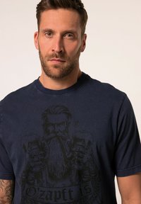 T-shirt in cotone blu navy con una grande grafica nera di un uomo barbuto che tiene in mano dei boccali di birra, con il testo "O'zapft Is" sottostante.