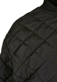 Gros plan de l'épaule d'une veste matelassée noire avec des surpiqûres en losange et un col côtelé.