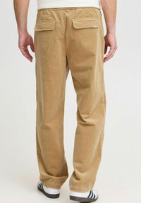 Beige Kordhosen mit geradem Schnitt, ausgestattet mit zwei Gesäßtaschen und einem strukturierten Stoff für Wärme und Komfort.