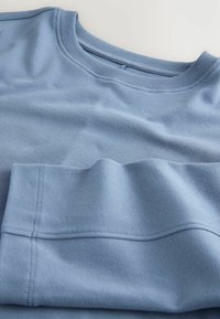 Pulover din bumbac de culoare albastru deschis, cu guler rotund, având o textură fină și detalii de cusătură vizibile pe margine și mâneci.