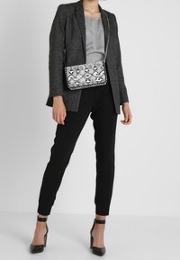 Grå texturerad kavaj över en silkesilver topp, i kombination med svarta tajta byxor och svarta högklackade skor. Silverhandväska med ormskinnsmönster.