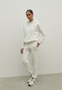 Biała bluza z kapturem i dresowe spodnie wykonane z miękkiego materiału, z kieszenią z przodu w bluzie i detalem z logo na spodniach.