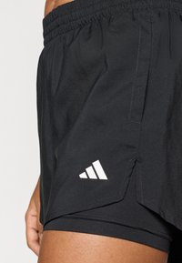 Schwarze Sportshorts mit elastischem Bund, versehen mit einem weißen Logo und seitlichen Schlitzen für Bewegungsfreiheit. Glattes, leichtes Material.