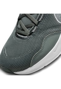 Zbliżenie na szary siateczkowy czubek sportowego buta z dopasowanymi sznurowadłami i białą podeszwą, z delikatnym wytłoczonym logo marki.