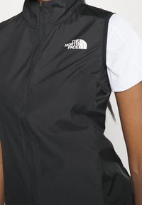 Svart väst i lättviktigt material, med hög krage, dragkedjestängning och logotypdetalj på vänster bröst. Ärmlös design med nätinslag.