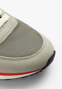 Grauer Sneaker aus einer Mischung aus Wildleder und Mesh. Abgerundete Form mit weißen und roten Akzenten, strukturierten Oberflächen und schwarzem Gummisohle.