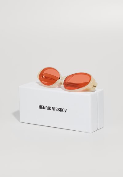 Raudoni objektyvo saulės akiniai su skaidriu kreminiu rėmu, ovalo formos. Pridedama balta dėžutė su užrašu "HENRIK VIBSKOV."