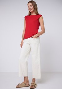 Haut rouge à manches courtes avec encolure bateau, associé à un pantalon large blanc et des sandales beige à enfiler avec des accents de boucle.