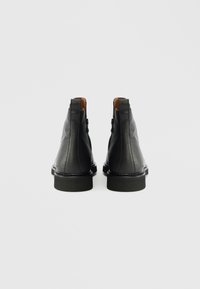 Svart skinn ankelstøvler med en jevn tekstur, rund tå, glidelåser på siden og en lav gummihæl. Kontraststing synlig langs sålen.