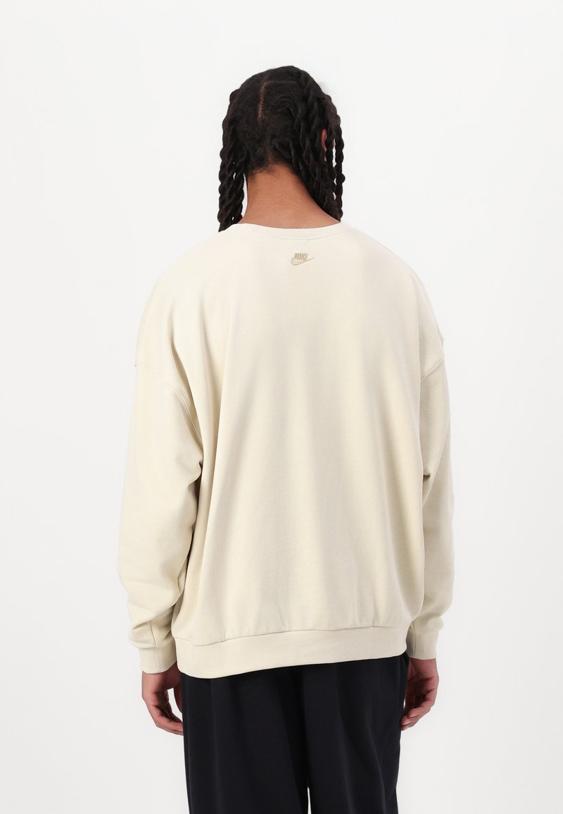 Sweatshirt couleur crème avec une coupe décontractée, des poignets et un ourlet côtelés ; présente un petit logo Nike doré dans le haut du dos.