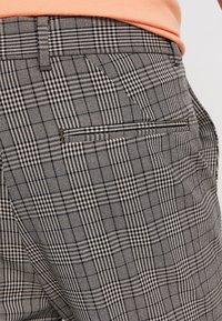 Grå mönstrade byxor har ett texturerat tyg med ett rutmönster, en rak front och en bakficka med dragkedjestängning.