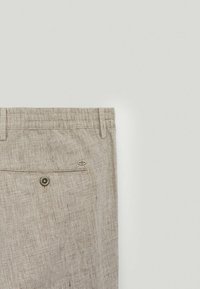 Pantalon en lin beige avec un motif à carreaux texturé, une taille élastique et une poche arrière fermée par un bouton en métal.