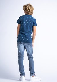 Tricou bleu marin cu mânecă scurtă, decorat cu modele mici verzi, asortat cu blugi albaștri deschiși și adidași albi. Design curat cu accente simple.
