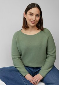 Lichtgroene lange mouwen trui met een ronde hals en een gestructureerd breipatroon, gecombineerd met blauwe denim broeken.