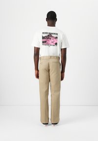 White cotton t-shirt with pink graphic print on back, paired with khaki pants. The pants have a straight cut and back pockets.