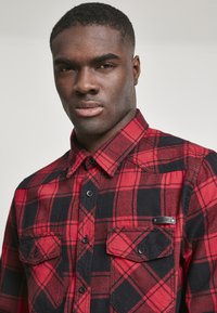 Rood en zwart geblokt flanellen shirt met een knoopsluiting aan de voorkant, twee borstzakken en een zwart label op de linkerzak. Geweven stof.