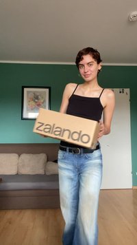Pappeske med "zalando" trykt i fete, svarte bokstaver. Personen som holder den har på seg en svart tank top og lyseblå falmede jeans.