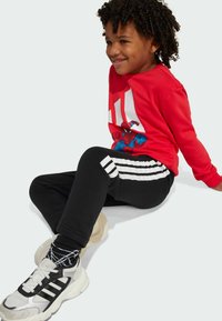 Red sweatshirt with Spider-Man graphic and white stripes, black track pants with white stripes, and gray athletic shoes with black accents.