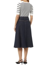 Dunkelblauer Denim-A-Linien-Rock mit Bund, verziert mit sichtbaren Nähten. Kombiniert mit einem gestreiften, figurbetonten Oberteil und schwarzen Slingback-Schuhen.