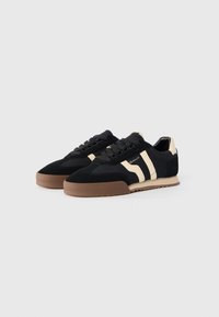 Black and cream sneakers with suede and textile upper, featuring a thick rubber sole, lace closure, and diagonal stripe accents.