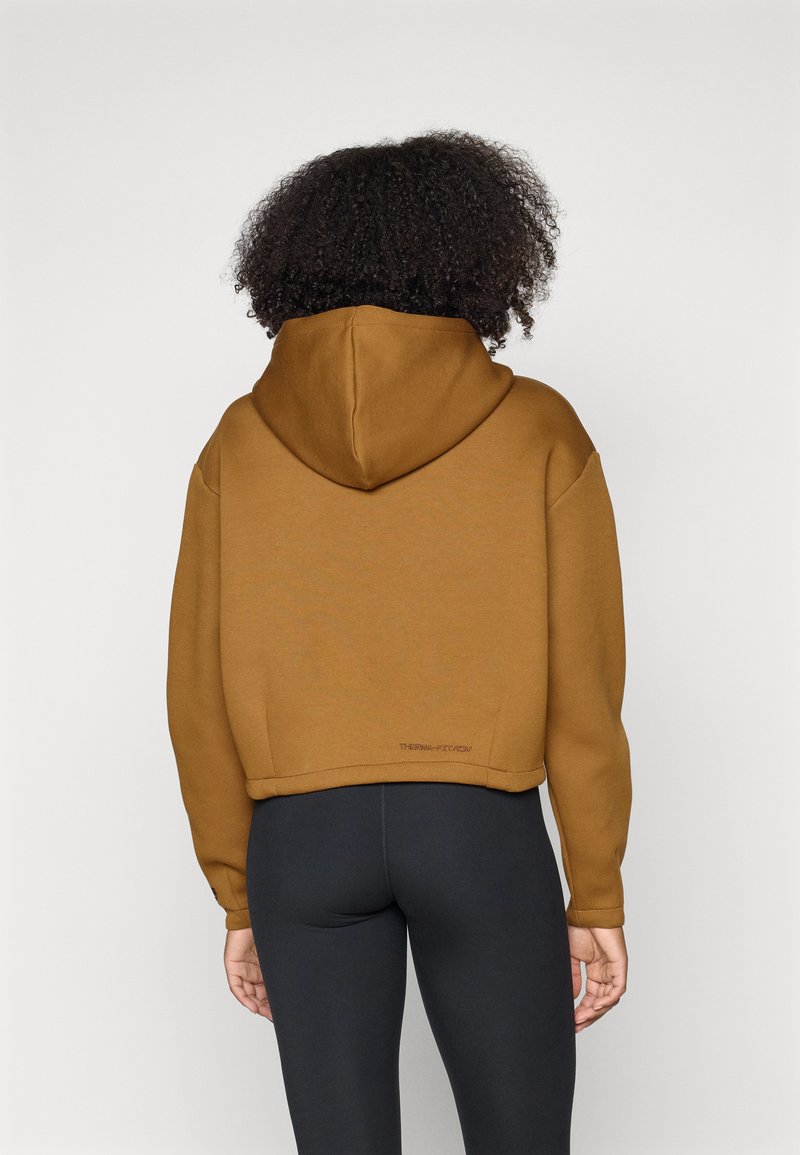 Braune, croppte Kapuzen-Sweatshirt aus weichem Material. Verfügt über eine Kängurutasche und gerippte Bündchen. Getragen mit schwarzen Leggings.