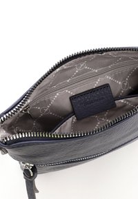 Mazs tumši zils ādas ķermeņa soma ar atvērtu augšējo rāvējslēdzēju, pelēkas rakstaina auduma oderi, iekšējo kabatu ar rāvējslēdzēju un zīmola etiķetes uzliku.