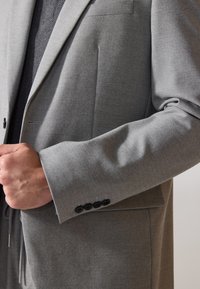 Grauern Sakko aus strukturiertem Stoff, mit einem Reverskragen, einer einzelnen Brusttasche und schwarzen Knopf-Akzenten an den Manschetten.