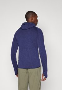 Hoodie à manches longues bleu marine avec une finition texturée, présentant un design ajusté, des trous pour les pouces et des coutures discrètes à l'arrière.