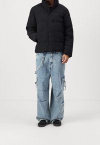 Chaqueta acolchada negra con cuello alto y costuras horizontales. Pantalones cargo de mezclilla de pierna ancha con múltiples bolsillos y lavado claro.