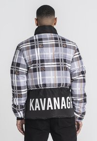 Padded jacket w kratę w odcieniach szaro-czarnych, z jednolitym czarnym dolnym fragmentem, na którym znajduje się tekst "KAVANAGH" w białym kolorze. Czarny kołnierz i detale z logo.